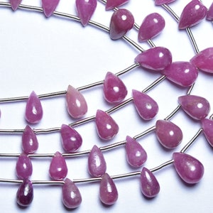 May include: A strand of pink gemstone beads in a teardrop shape. The beads are strung on silver wire.