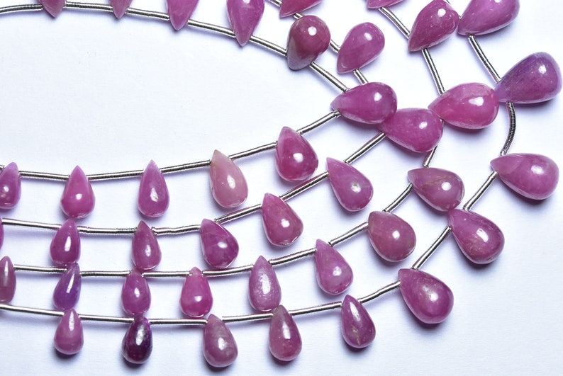 May include: A strand of pink gemstone beads in a teardrop shape. The beads are strung on silver wire.