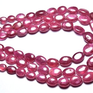 May include: A strand of pink ruby gemstone beads. The beads are oval shaped and have a smooth, polished finish.