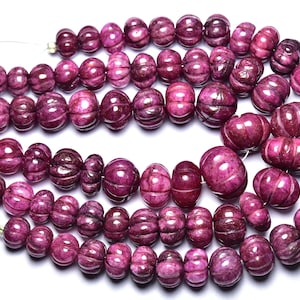 Può includere: Fili di perline di pietre preziose magenta scuro intagliate. Le perline hanno una forma a zucca con scanalature verticali. Le perline sono infilate su un filo sottile e trasparente. Le perline sono di un colore magenta intenso e ricco.