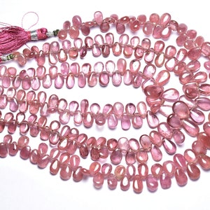 Può includere: Una collana di perle di pietre preziose rosa, ogni perla ha una forma a goccia. Le perle sono infilate su un filo sottile e hanno un fiocco ad ogni estremità.