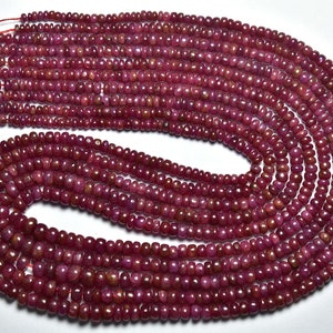 Pode incluir: Um fio de contas de pedras preciosas de cor vermelha rubi. As contas são pequenas e redondas, e são enfiadas em um fio fino. As contas são dispostas em um padrão circular, e todas são do mesmo tamanho e forma.