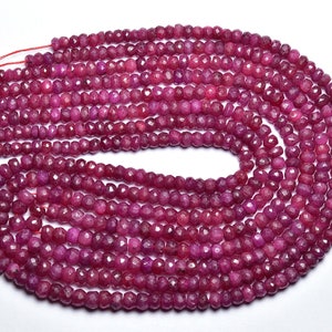 May include: A strand of ruby red faceted gemstone beads. The beads are small and round, and they are strung on a thin thread. The beads are arranged in a circular pattern, and they are all the same size and shape.