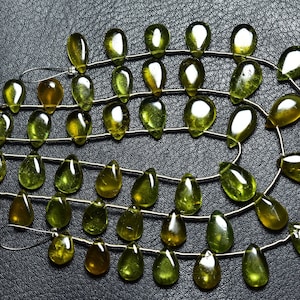 May include: A strand of green gemstone beads in a teardrop shape. The beads are strung on a silver wire and are arranged in a circular pattern.