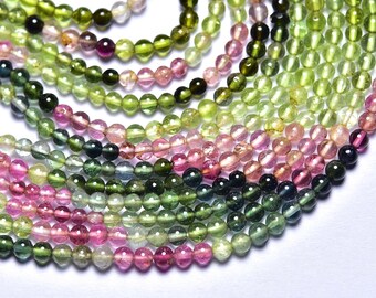 May include: A strand of round, multi-colored gemstone beads. The beads are shades of pink, green, and blue. The beads are arranged in a graduated pattern, with the pink beads at the bottom and the green beads at the top.