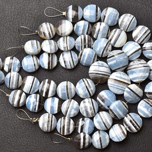 May include: A collection of round, faceted beads arranged in multiple strands. Each bead features a light blue and white base with distinct, parallel dark brown or black stripes running across the surface. The beads are strung on thin wire.