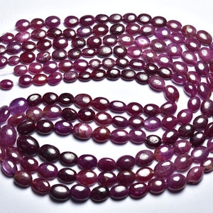 Peut inclure: Un brin de perles de rubis de forme ovale, de couleur rouge foncé, disposées en cercle sur un fond blanc.