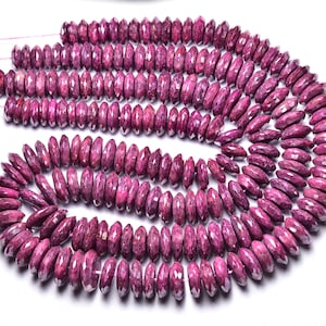 Può includere: Una collana di perle di rubino, ogni perla è sfaccettata e ha una forma leggermente ovale. Le perle sono di un colore rosso intenso e ricco.
