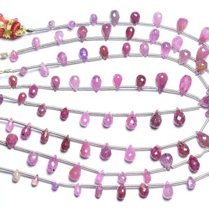 Puede incluir: Una hebra de cuentas de piedras preciosas rosas en forma de lágrima. Las cuentas están enhebradas en alambre plateado y están dispuestas en varias filas.