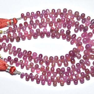 Può includere: Fili di perline di pietre preziose rosa-viola a forma di goccia. Le perline sono infilate insieme, formando collane. Nappe rosse con dettagli argentati sono visibili alle estremità. Le pietre preziose hanno una finitura lucida. Misurate in cm.