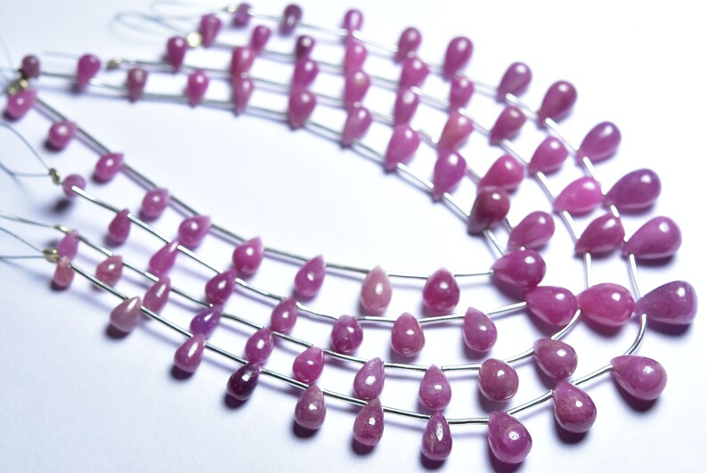 May include: A strand of pink gemstone beads, each bead is a teardrop shape and strung on a silver wire.