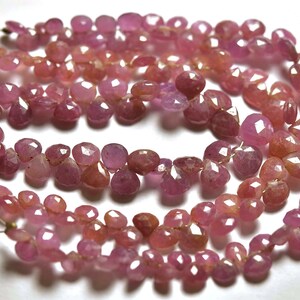 May include: A strand of pink gemstone beads, likely ruby, with a faceted, teardrop shape. The beads are strung on a thin wire and are arranged in a loose, flowing pattern.