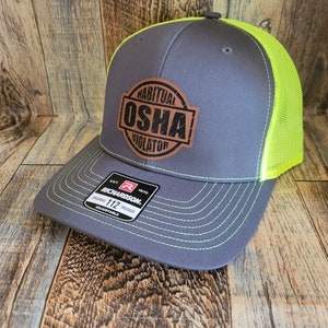 Könnte beinhalten: Eine graue und neongelbe Trucker-Kappe mit einem braunen Leder-Patch, auf dem "Habitual OSHA Violator" steht.