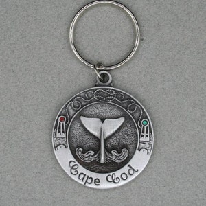 May include: Silver keychain with a round charm featuring a whale tail and the words "Cape Cod". The charm has red and green accents.