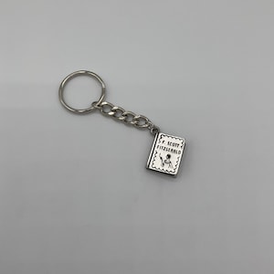 May include: Silver keychain featuring a small book charm with the text "F. Scott Fitzgerald" on the cover.