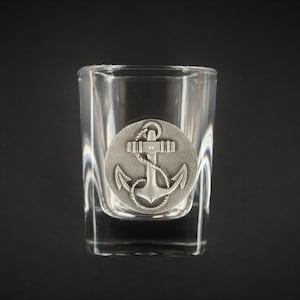 Puede incluir: Un vaso de chupito de vidrio transparente con un diseño de ancla de plata en la parte delantera.