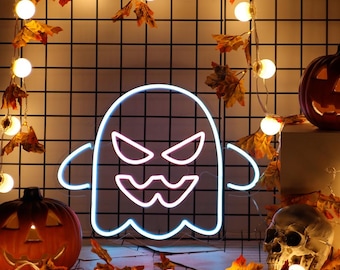 May include: A white neon ghost sign with a glowing outline, featuring sharp triangular eyes and a jagged mouth. The ghost is positioned against a black wire grid backdrop decorated with warm string lights, autumn leaves, a pumpkin, and a skull.