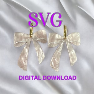 Puede incluir: Un par de pendientes de lazo blanco con aros dorados. Los lazos tienen un efecto marmoleado y son de un diseño delicado. DESCARGA DIGITAL SVG.