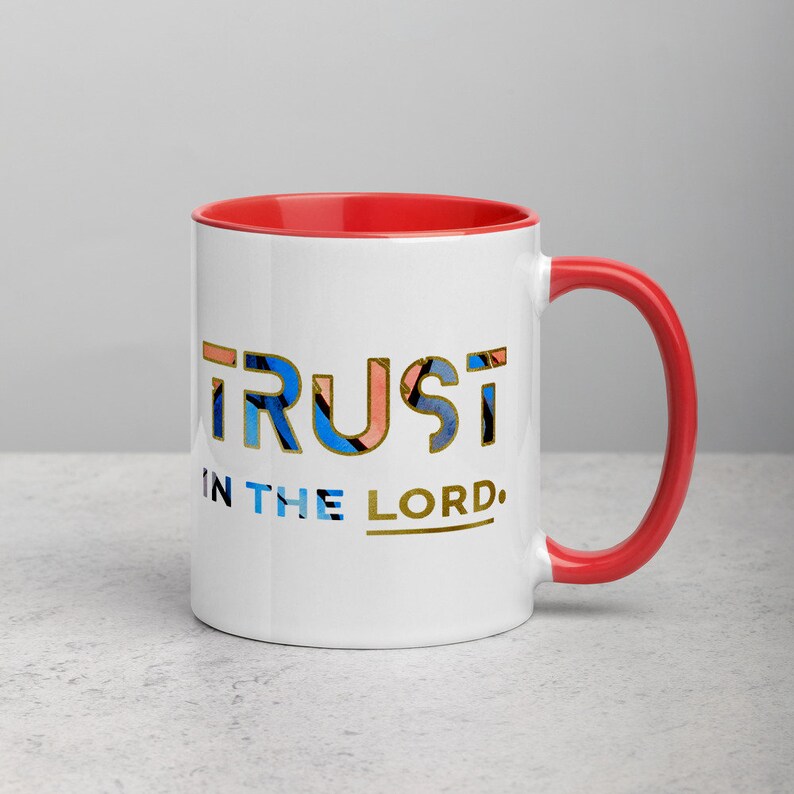Pu&ograve; includere: Tazza in ceramica bianca con bordo e manico rossi. La tazza presenta un design dorato che dice "TRUST IN THE LORD."