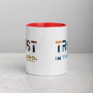 Pu&ograve; includere: Tazza in ceramica bianca con bordo rosso. La tazza presenta il testo "Just Trust in the Lord." in un font geometrico colorato.