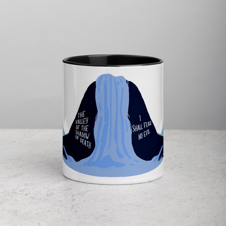 May include: White ceramic mug with a black rim and handle. The mug features a blue and black illustration of a waterfall with the text "The Valley of the Shadow of Death" on the left side and "I Shall Fear No Evil" on the right side.