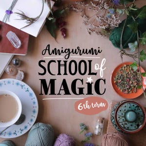 以下が含まれることがあります： 薄い茶色の背景に黒い文字で「Amigurumi School of Magic 6th term」と書かれたフラットレイ画像。画像には糸、お茶、クリスタル、その他のクラフト用品が含まれています。