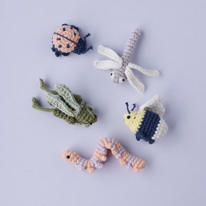 Może przedstawiać: Pięć pluszowych zabawek w kształcie zwierząt: biedronka, ważka, konik polny, trzmiel i robak. Zabawki są wykonane z przędzy w różnych kolorach i mają szczegółowe cechy.