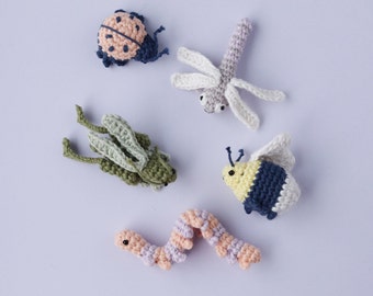 May include: Five crocheted animal toys: a ladybug, a dragonfly, a grasshopper, a bumblebee, and a worm. The toys are made with different colored yarn and have detailed features.