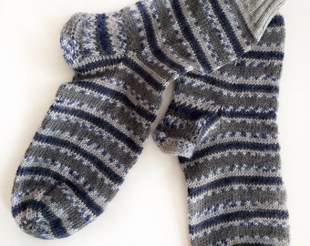 Könnte beinhalten: Ein Paar graue und blaue gestreifte Socken mit einem grauen Bündchen. Die Socken sind gestrickt und haben ein dezentes Muster.