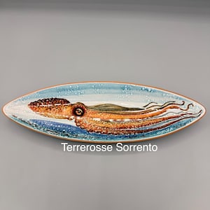 Puede incluir: Un plato de cerámica ovalado y alargado con un pulpo pintado a mano en tonos naranja y marrón sobre un fondo azul claro texturizado. El borde es de color terracota natural. El texto Terrerosse Sorrento aparece debajo del plato.
