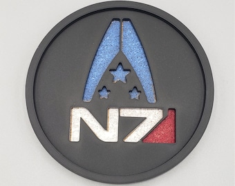 May include: A circular black coaster featuring a cutout design of the N7 logo. The emblem includes a blue textured background behind the upper triangular shape with three stars and a red textured background behind the number 7.