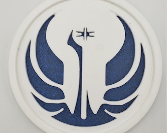 May include: White round coaster with a blue and white symbol of a stylized bird with wings spread. The symbol is surrounded by a white border.