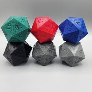 Puede incluir: Seis dados poliédricos en varios colores: verde azulado, rojo, azul, negro, gris y plateado. Cada dado tiene veinte caras con números grabados. Los dados están dispuestos en dos filas de tres.