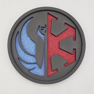 Op de afbeelding: Een ronde zwarte en grijze onderzetter met een rood en blauw symbool. Het symbool is een gestileerde weergave van de Rebel Alliance en het Galactic Empire uit Star Wars.
