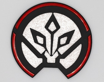 May include: A black and white stylized design of a creature with a red ring around the outside. The design is on a round, black coaster.