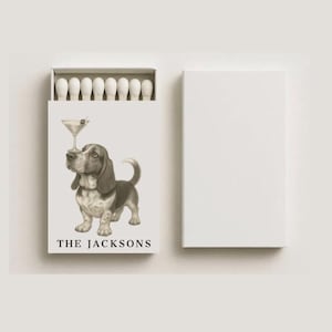 May include: A white matchbox with a Basset Hound illustration balancing a martini glass. The box is open, revealing white match heads. The text "THE JACKSONS" is printed below the dog illustration. A separate, blank white box is also present.