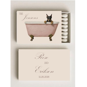 May include: Matchbox with a light pink background. The top of the matchbox features a dog in a bathtub with the text "The Jensons". The bottom of the matchbox has the text "Rose and Erikson" and the date "12.26.2026".