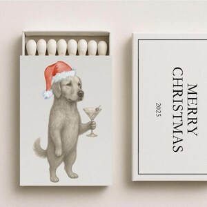 May include: A matchbox set with a festive theme. The matchbox features a watercolor illustration of a golden retriever wearing a Santa hat and holding a martini. The box next to it reads "MERRY CHRISTMAS 2025".