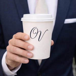 May include: A white ceramic mug with a black handle and the text "But First, Coffee" in a bold, black font. The mug sits on a white surface, showcasing its clean design.