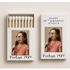 Könnte beinhalten: Zwei weiße Streichholzschachteln, eine offen mit Streichhölzern, mit einem Foto eines Mädchens mit Brille und Mikrofon. Auf einer steht "Vintage 1984", auf der anderen "Happy 40th Birthday Jessica" und "Vintage 1984".