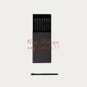May include: A black matchbox filled with black matches, with one match lying separately below. The text "Any Design any colors!!" is written in red cursive font.