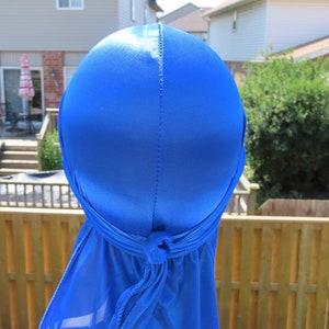 Puede incluir: Un durag de satén azul real con una cola larga. El durag está atado en la parte posterior de la cabeza.