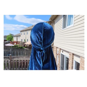May include: A blue velvet durag with a tied knot at the back. The durag is worn on a person's head.