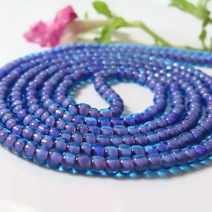 May include: A close-up of a strand of blue and purple glass beads. The beads are small and round, and they are arranged in a spiral pattern.