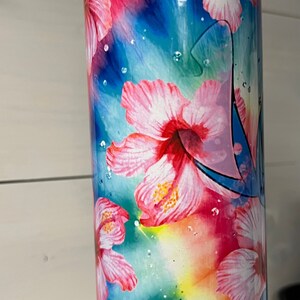 Puede incluir: Un vaso de acero inoxidable con un dise&ntilde;o de tie-dye colorido con flores de hibisco rosas y un personaje de dibujos animados azul.