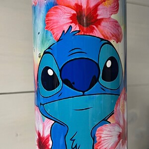 Puede incluir: Un vaso de acero inoxidable con un dise&ntilde;o floral colorido en rosa, amarillo y naranja. El personaje de Stitch, azul y turquesa, de Lilo & Stitch est&aacute; representado en el vaso.