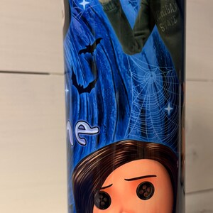 May include: A stainless steel tumbler featuring characters from the animated film "Coraline." The design includes images of Coraline, the Other Father, bats, and spiderwebs against a blue starry background. The tumbler has a black lid.