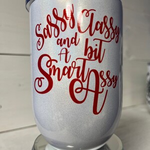 May include: White tumbler with a red glitter finish and red vinyl lettering that reads "Sassy Classy and a bit Smart Assy".