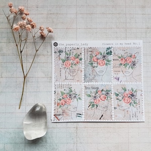 Könnte beinhalten: Ein Bogen mit sechs floralen Aufklebern mit Strichzeichnungen von Gesichtern, die mit Blumenkränzen geschmückt sind. Die Aufkleber haben eine Vintage-Ästhetik mit Text und einer sanften Farbpalette aus Rosa, Grün und Beige. Der Text "flowers in my head No.1" ist sichtbar.