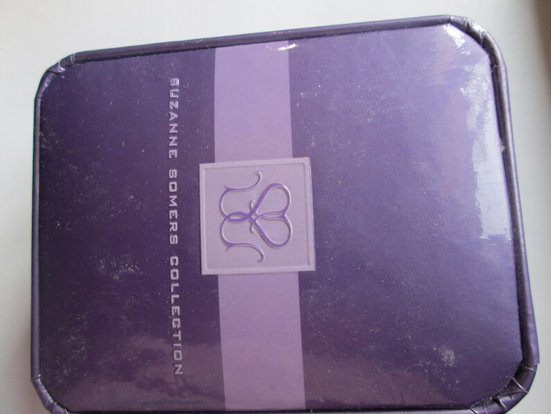 May include: A purple box with the text "SUZANNE SOMERS COLLECTION" and a logo of two intertwined hearts.
